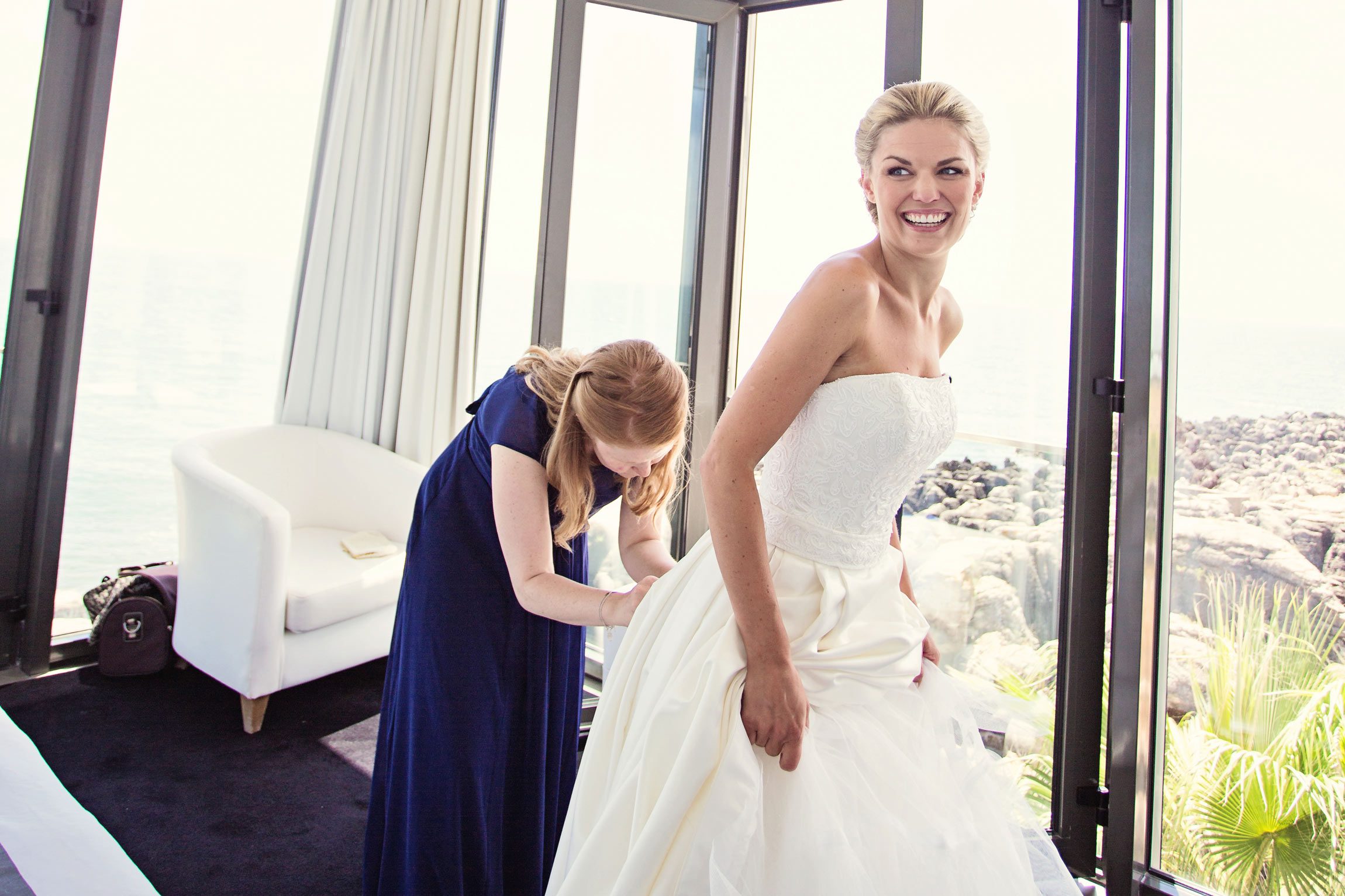 white bride getting her wedding dress on with the help of her sister