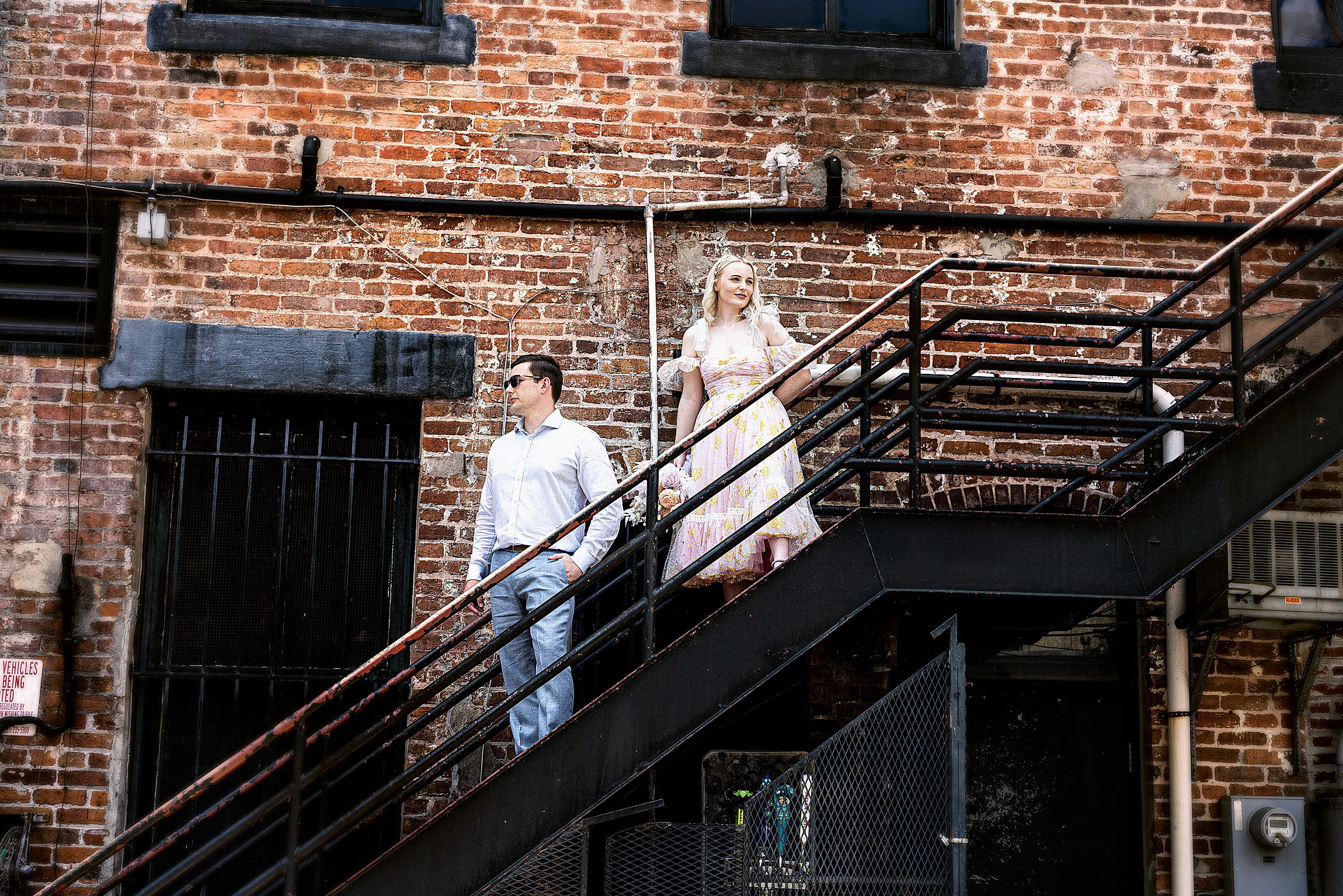 white couple standing on a metal staircase outdoors in front of a brick wall in downtown orlando after their orange county courthouse wedding
