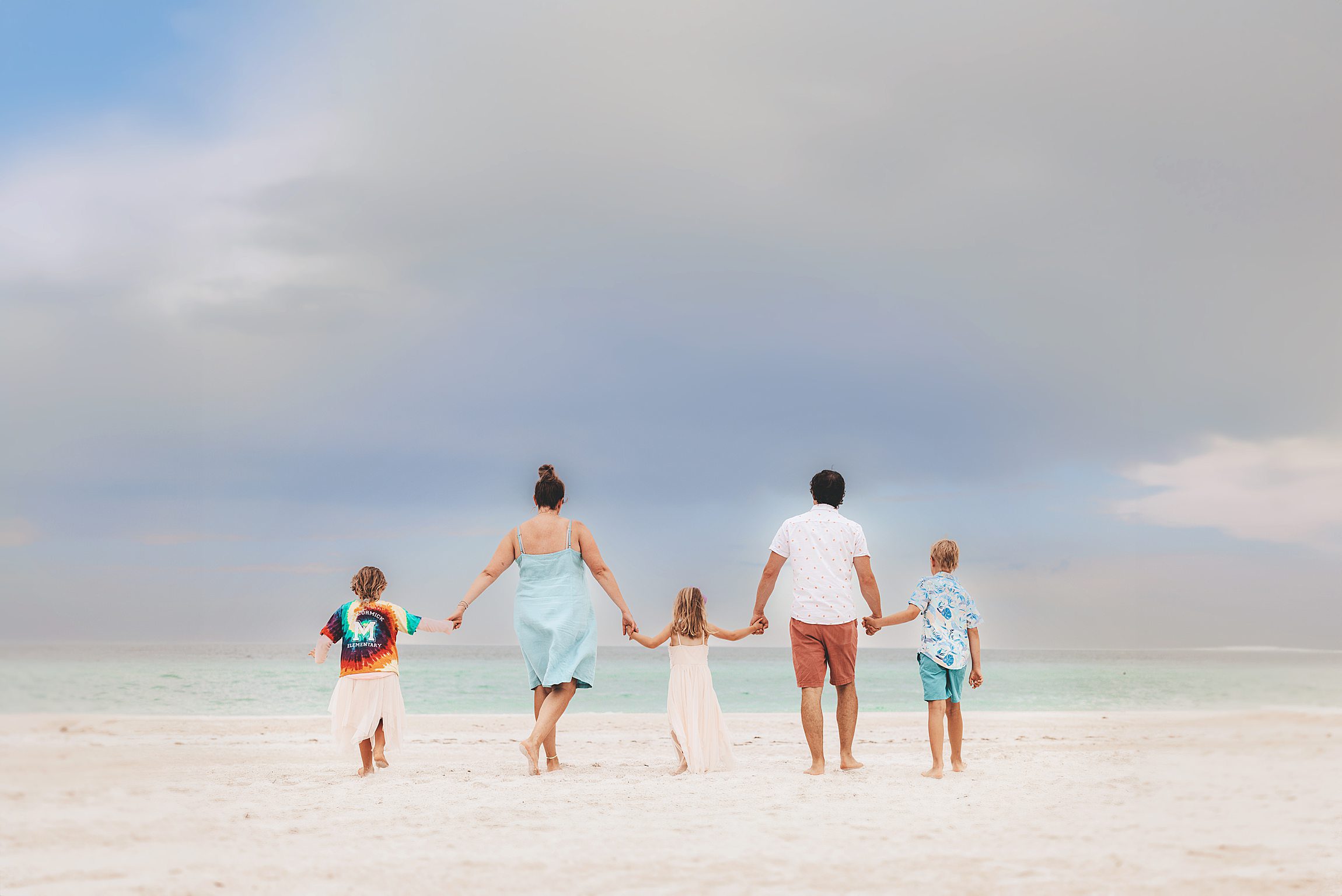 family of two adults and three kids walking toward the shore on the beach on anna maria island