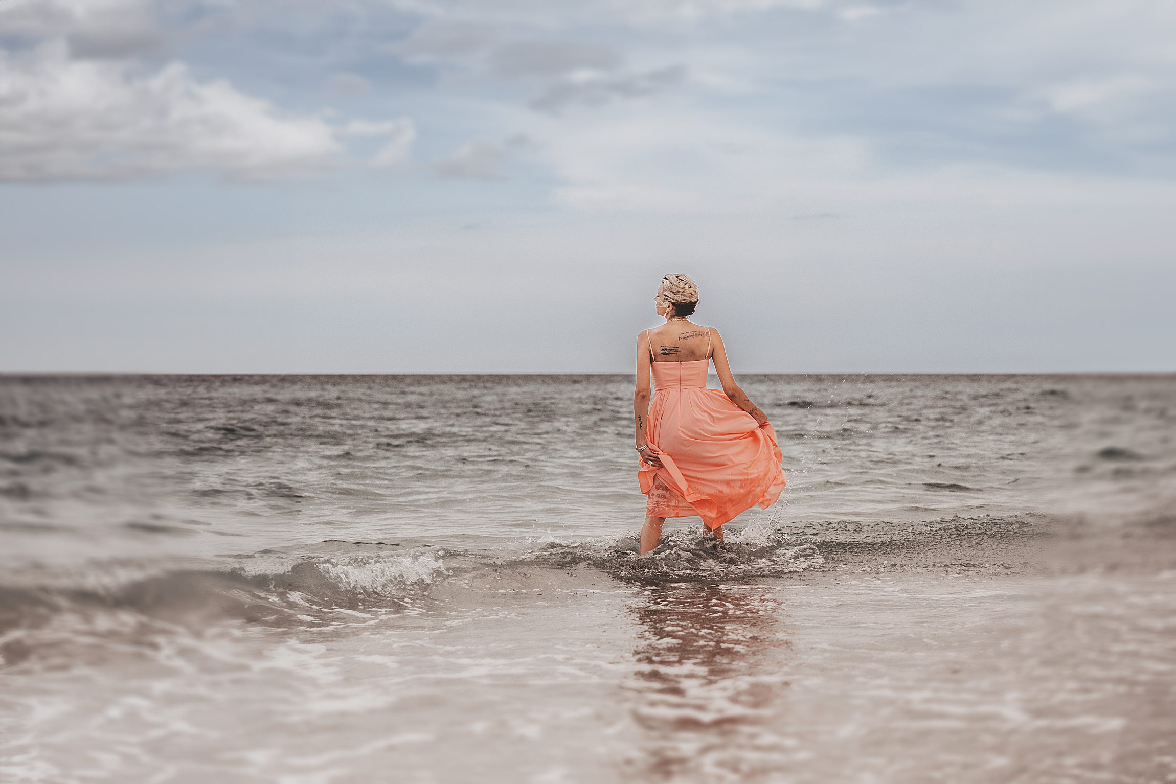 woman in a coral dress standing knee-deep in the ocean on anna maria island