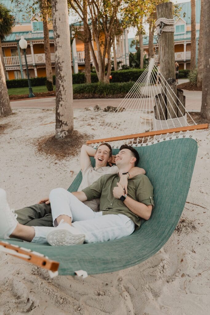 LGBTQIA+ elopement portrait of two grooms wearing casual tan and brown outfits on a teal hammock on the beach at an Orlando Florida resort, captured by Gracie May Photography