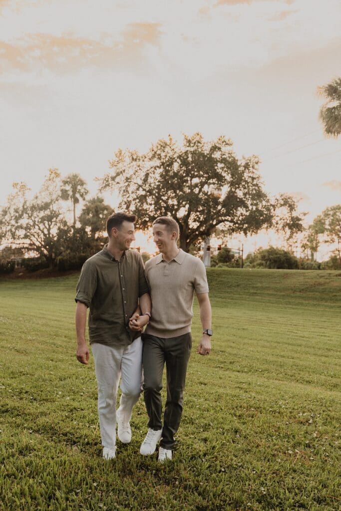 LGBTQIA+ elopement portrait of two grooms wearing casual tan and brown outfits on a grassy lawn at sunset at an Orlando Florida resort, captured by Gracie May Photography