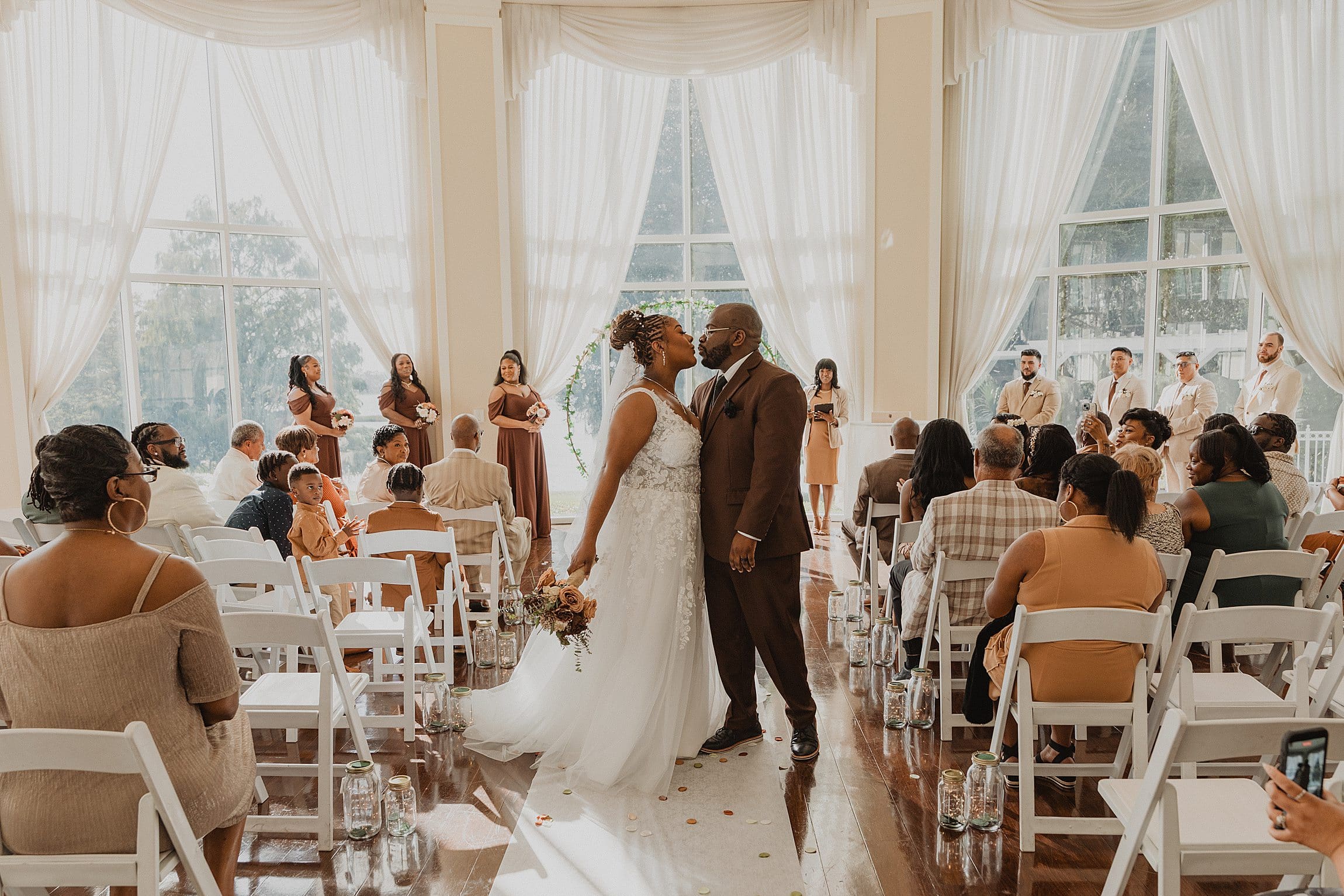 bride wearing white and groom wearing a chocolate brown suit kiss while walking back down the aisle after their ceremony in the rotunda at Lake Mary Events Center in Florida, captured by Gracie May Photography