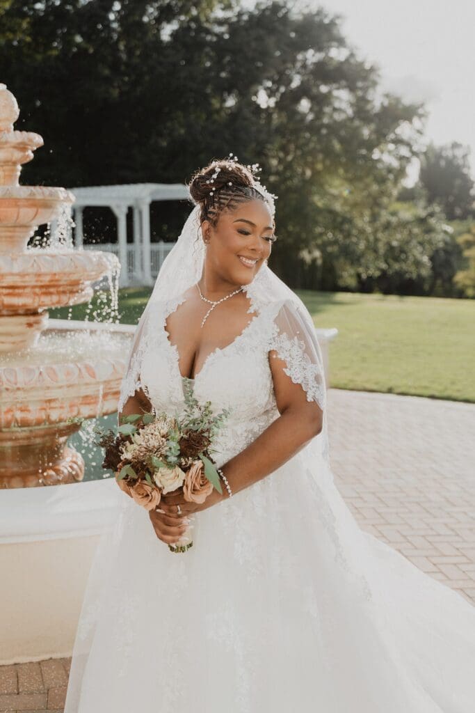 bride holding her bouquet of brown and tan flowers in front of a tiered fountain on the lawn at Lake Mary Events Center in Florida, captured by Gracie May Photography