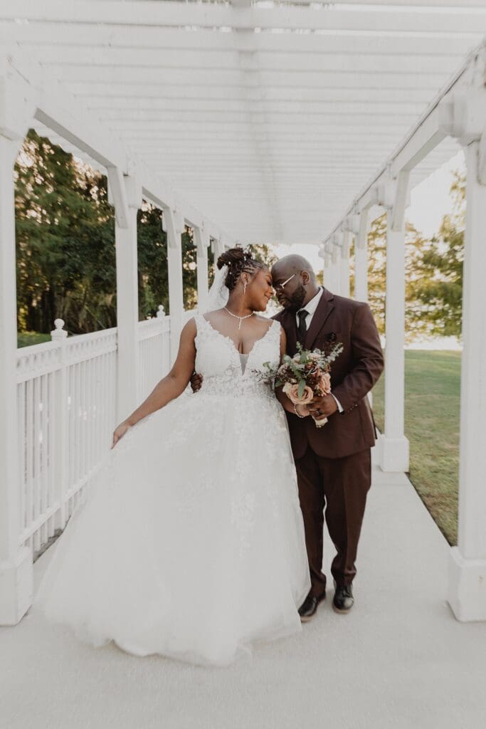 bride wearing white and groom wearing a chocolate brown suit walk under a white trellis on the lawn at Lake Mary Events Center in Florida, captured by Gracie May Photography