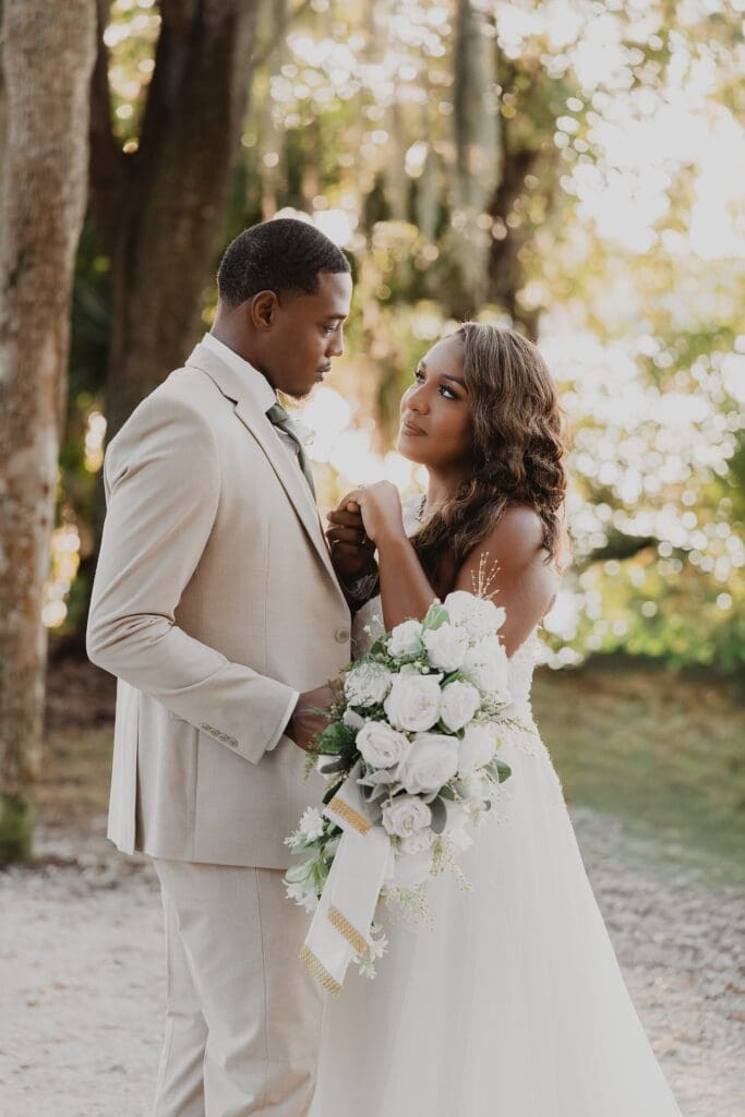 bride and groom look at each other lovingly holding a bouquet of quite roses during sunset golden hour at Kraft Azalea Garden in Winter Park, Florida, captured by Gracie May Photography
