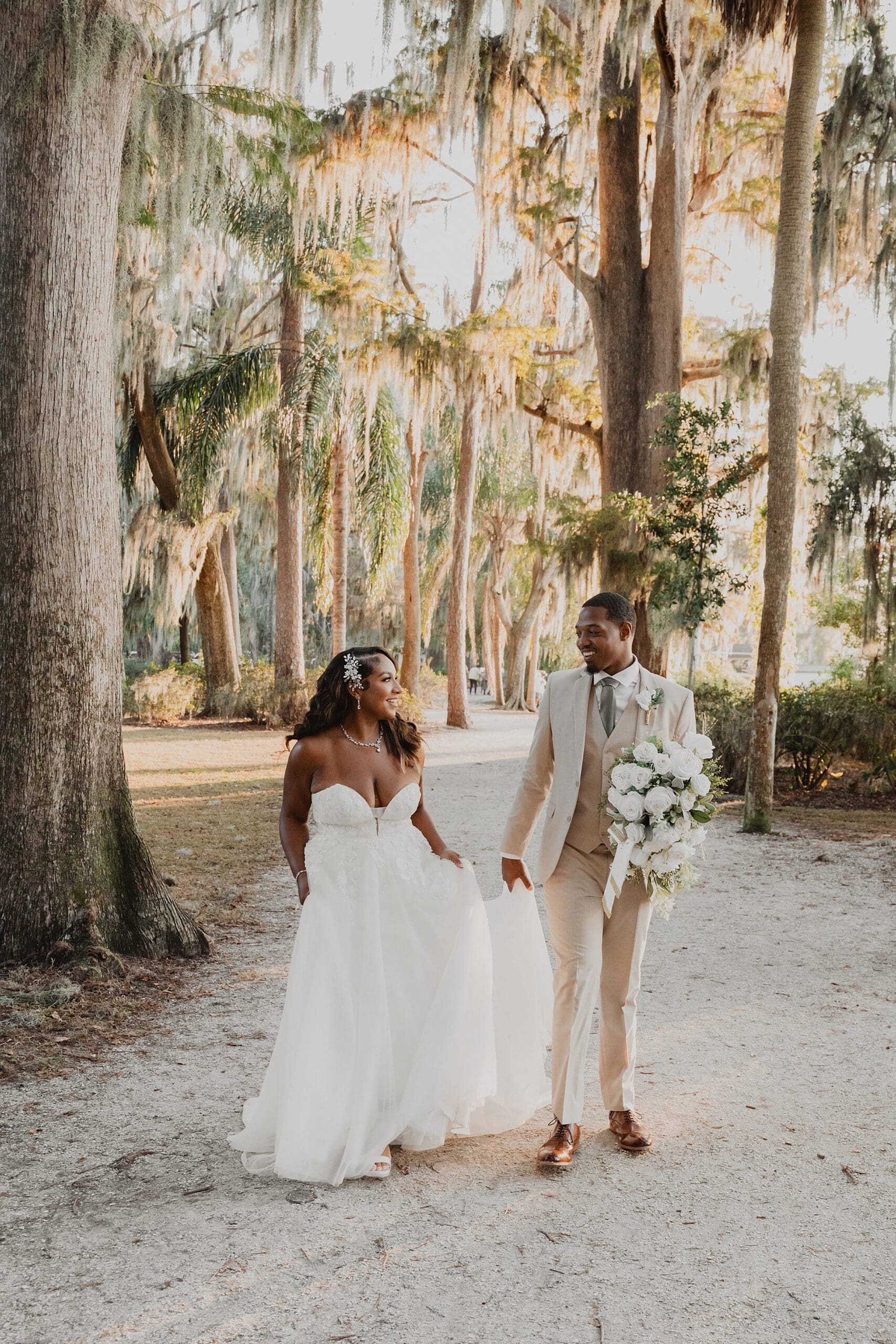 bride and groom walking on a path underneath trees during sunset golden hour at Kraft Azalea Garden in Winter Park, Florida, captured by Gracie May Photography