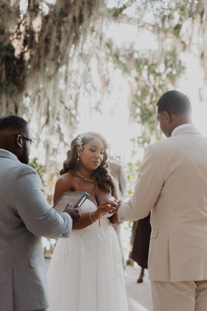 bride putting a wedding ring on her groom at the Exedra Monument during their sunset golden hour micro wedding ceremony at Kraft Azalea Garden in Winter Park, Florida, captured by Gracie May Photography