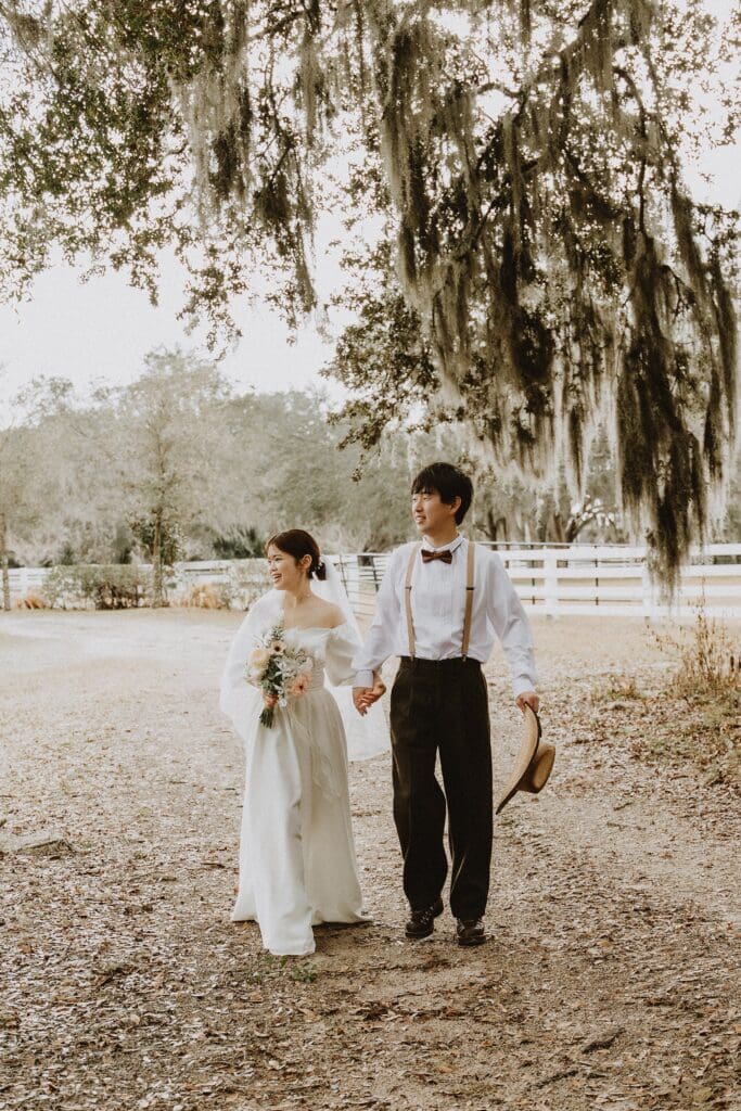 bride and groom in a wedding dress and western wear walking in a grassy pasture at Horsepower Ranch in Geneva, Florida, captured by Gracie May Photography