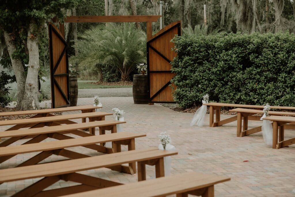 outdoor ceremony space on a brick patio with wooden benches and a wooden gate The Venue at Gentry Pines, captured by Gracie May Photography