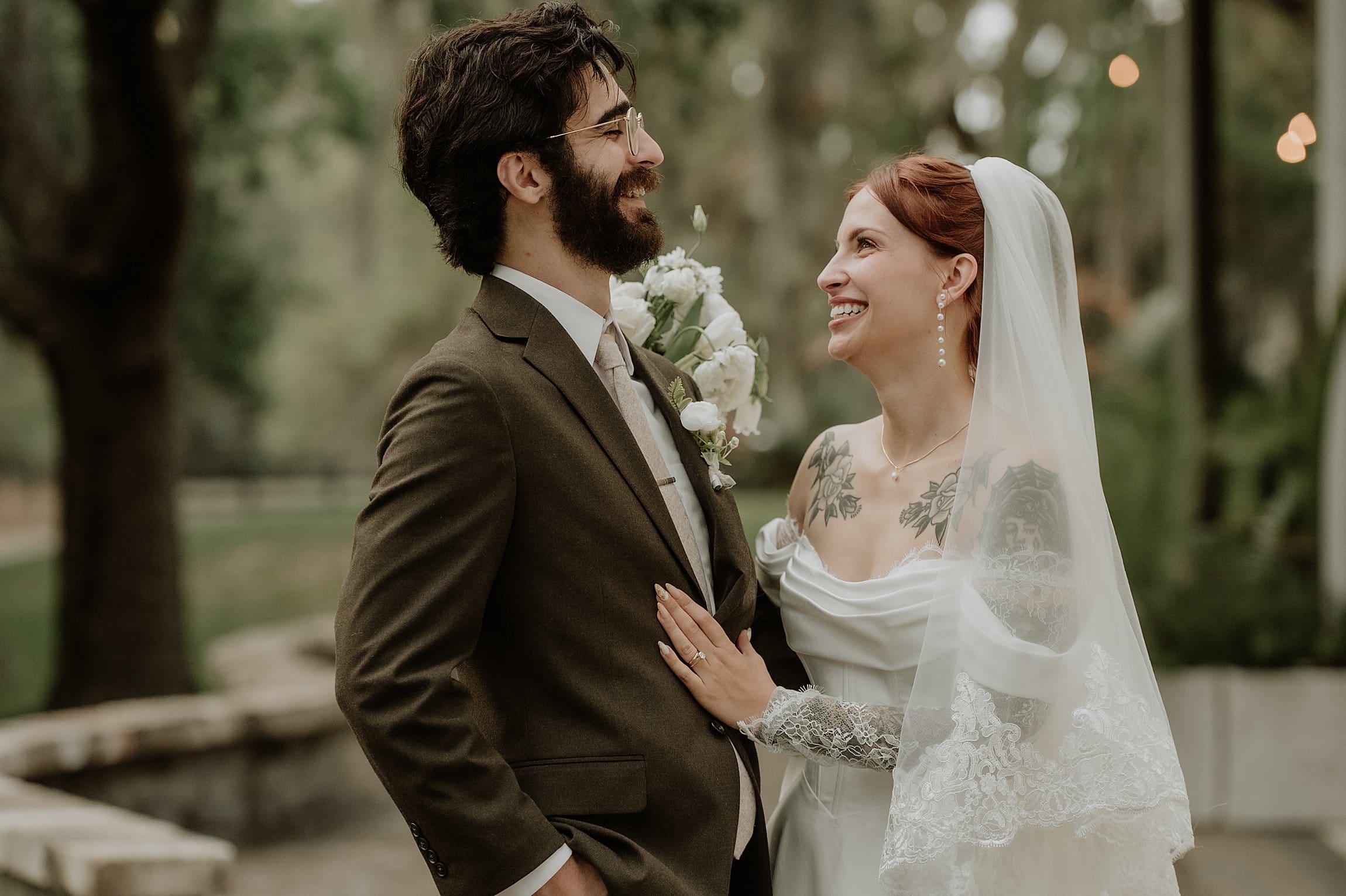 groom in brown suit and bride in an off-the-shoulder gown smile at each other at this vintage style rainy day wedding at The Venue at Gentry Pines, captured by Gracie May Photography