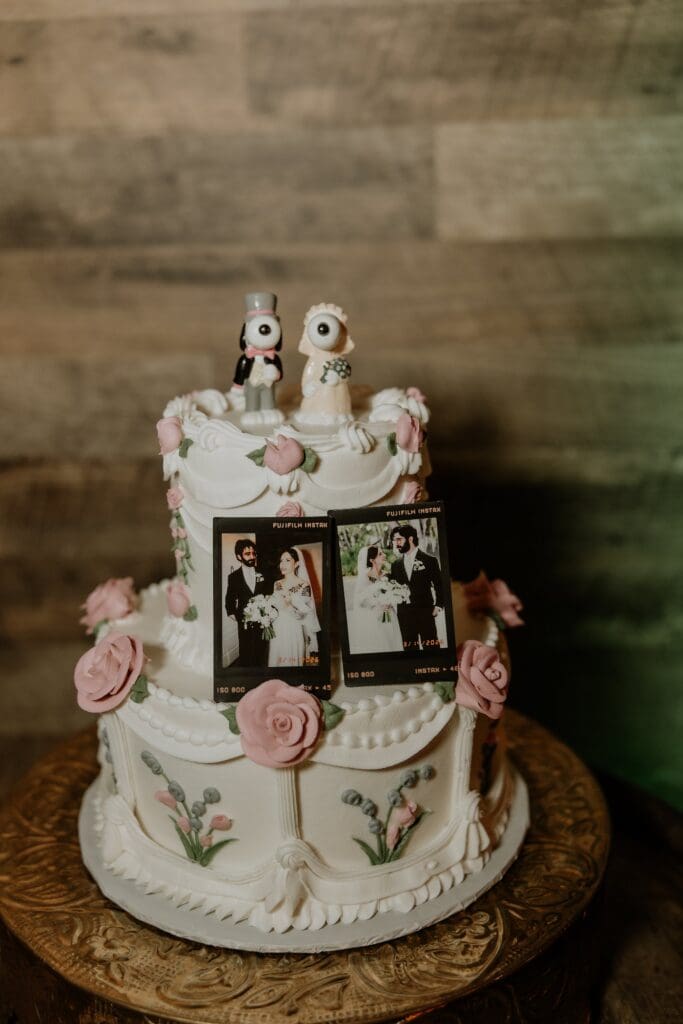 two-tiered white wedding cake with bluse rose details decorated with poloroid photos of the couple at this vintage style rainy day wedding at The Venue at Gentry Pines, captured by Gracie May Photography