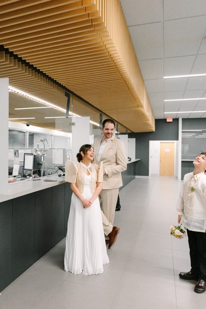bride in a white dress with a Filipino style jacket and groom in a tan linen suit wait for a marriage license at the Winter Park Clerk of Courts with their kids, captured by Gracie May Photography