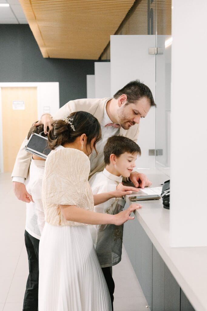 bride in a white dress with a Filipino style jacket and groom in a tan linen suit apply for a marriage license at the Winter Park Clerk of Courts with their kids, captured by Gracie May Photography