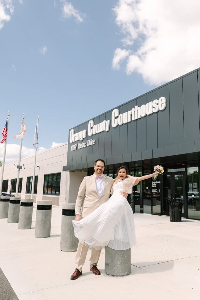 bride in a white dress with a Filipino style jacket and groom in a tan linen suit pose outside the Orange County Courthouse in Winter Park after their courthouse wedding, captured by Gracie May Photography