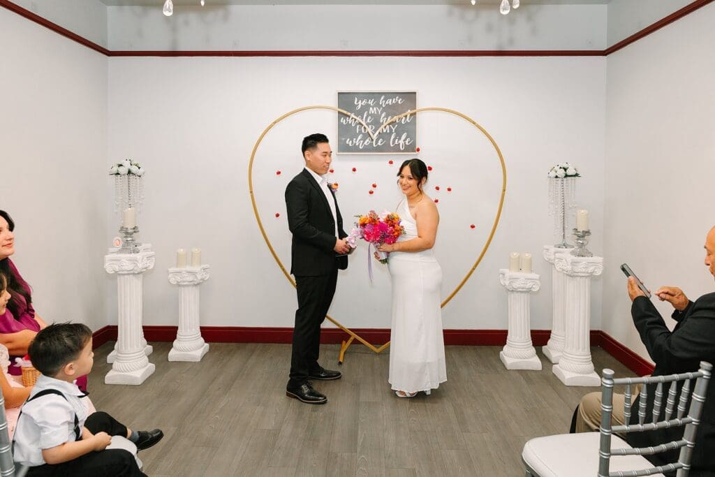bride and groom in formal wedding attire carrying a bright spring bouquet in the ceremony room at Orange County Courthouse in Orlando during their courthouse wedding, captured by Gracie May Photography.