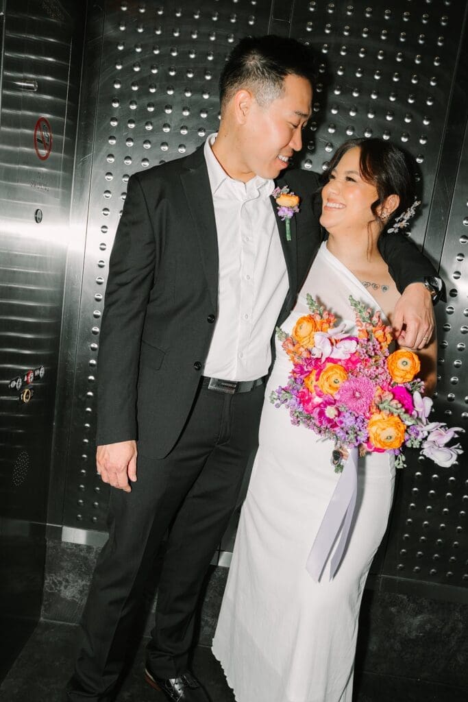 flash shot of a bride and groom in formal wedding attire with a bright spring bouquet laughing in the elevator at the Orange County Courthouse in Orlando, captured by Gracie May Photography.