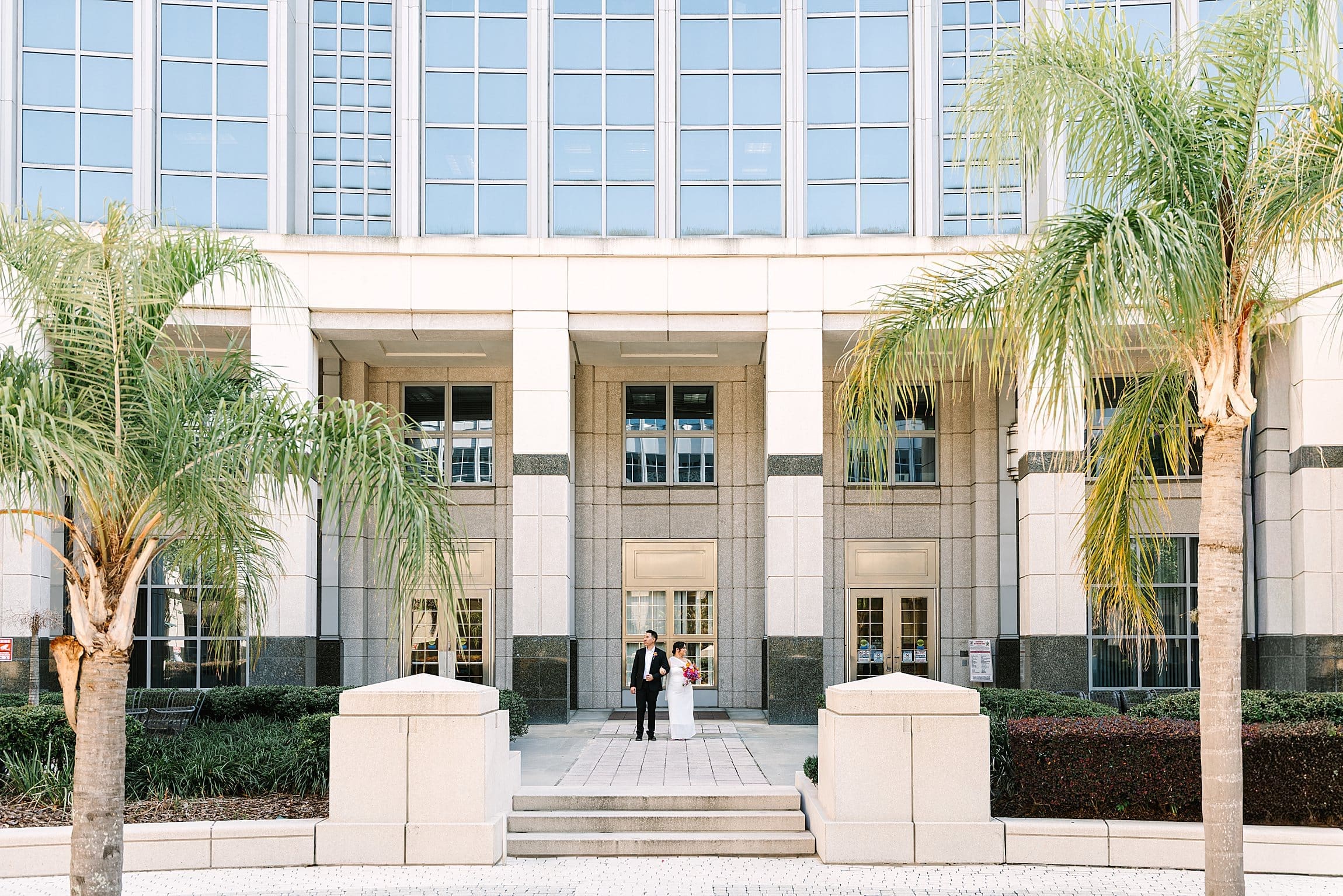 bride and groom in formal wedding attire carrying a bright spring bouquet in front of the Orange County Courthouse in Orlando after their courthouse wedding, captured by Gracie May Photography.