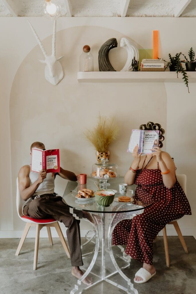 pregnant woman and man holding up What to Expect when You're Expecting during their retro lavender pregnancy maternity photoshoot captured by Gracie May Photography