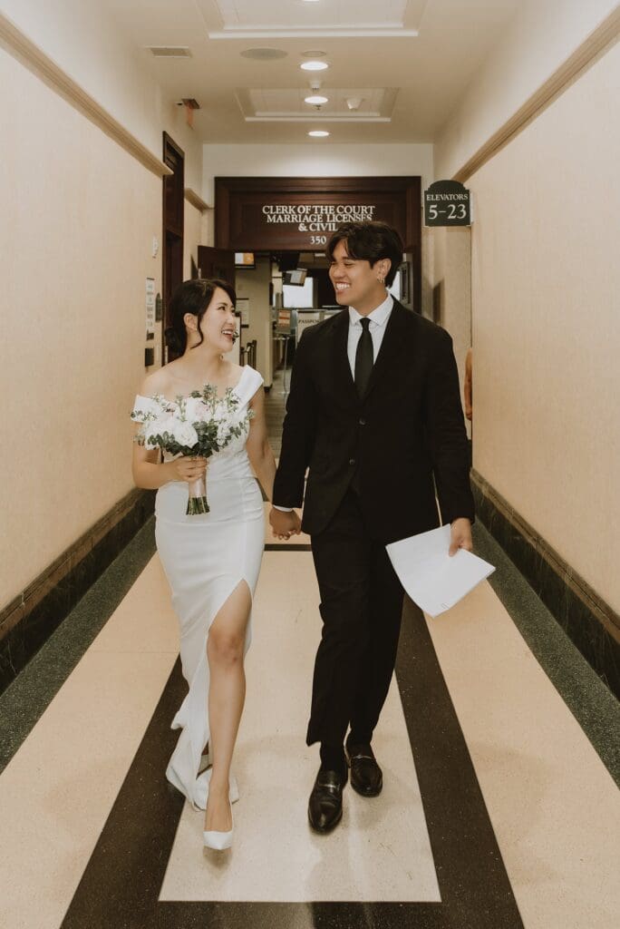 bride and groom walk holding hands in the corridor inside the Orlando Orange County Courthouse, captured by Gracie May Photography