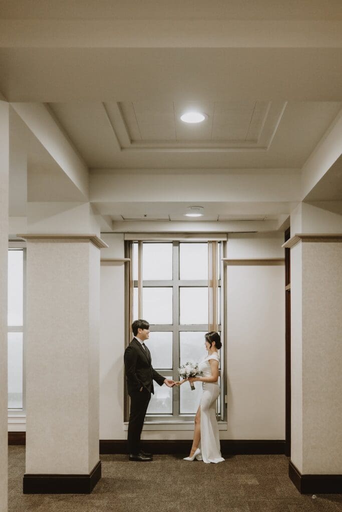 bride and groom stand by a large window holding hands inside the Orlando Orange County Courthouse, captured by Gracie May Photography