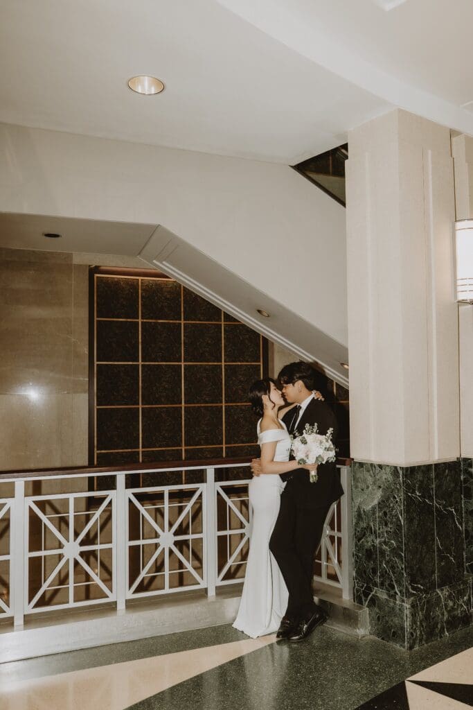 bride and groom kiss by a marble column inside the Orlando Orange County Courthouse, captured by Gracie May Photography