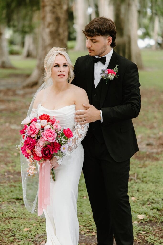 bride and groom wearing classic black and white wedding attire with a bold red and pink bouquet at an elopement at Kraft Azalea Garden in Winter Park, Florida, captured by Gracie May Photography