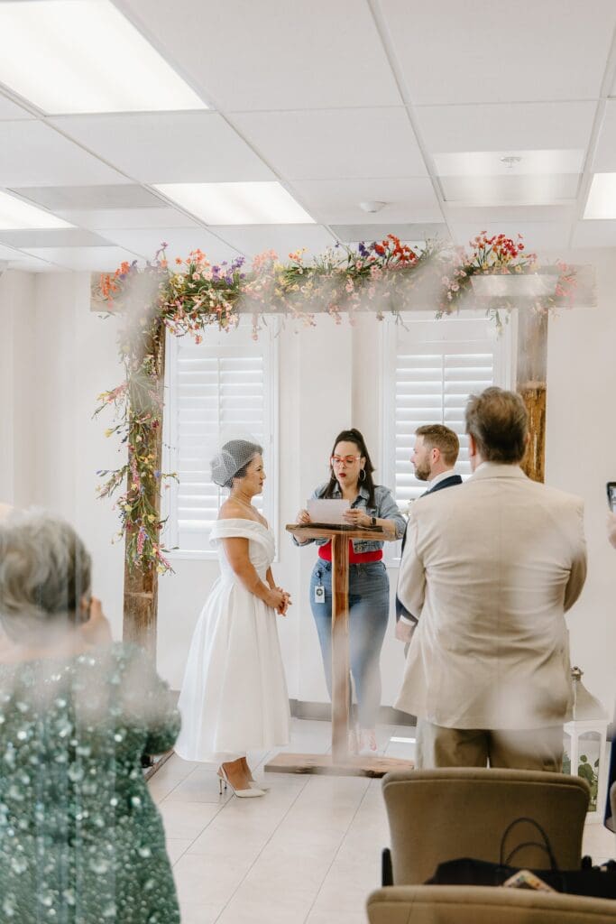 bride and groom get married under a wooden arch with wildflowers in the ceremony room at St. Lucie County Clerk of Courts in Florida, captured by Gracie May Photography