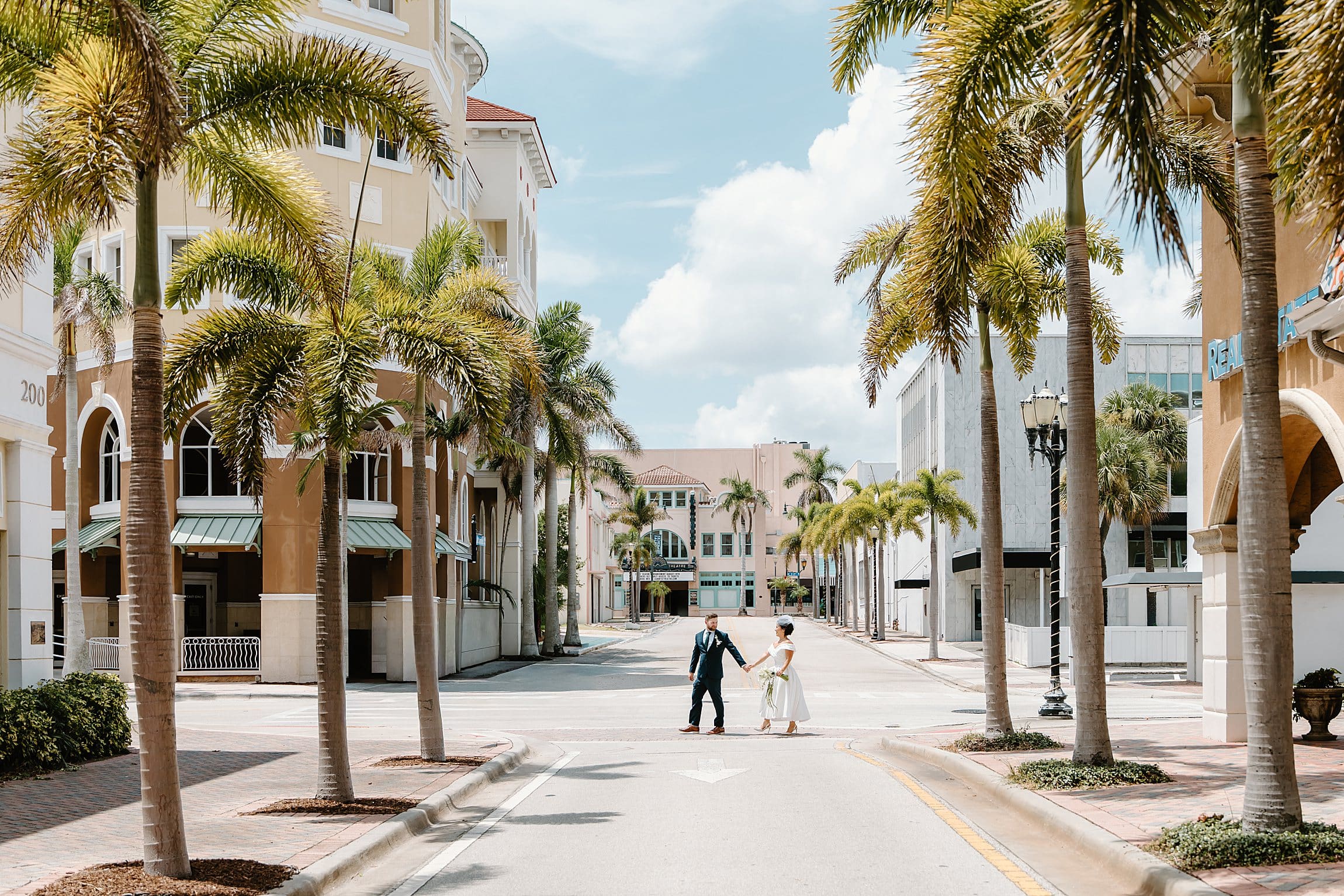 wide shot of bride and groom walking across a palm-tree-lined street in downtown Fort Pierce, Florida, captured by Gracie May Photography