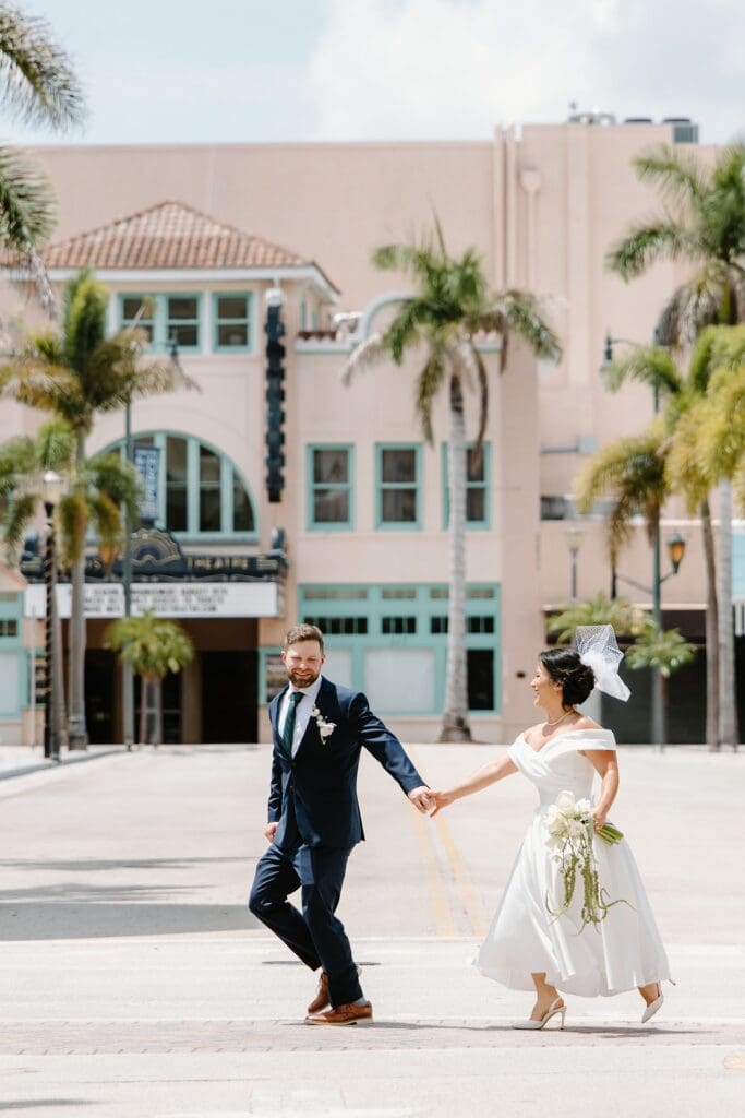 bride and groom walk playfully across the street in front of the Sunrise Theatre in downtown Fort Pierce, Florida, captured by Gracie May Photography