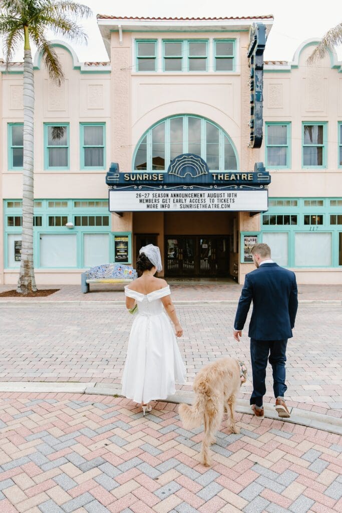 bride and groom walk with their dog in front of the Sunrise Theatre in downtown Fort Pierce, Florida, captured by Gracie May Photography
