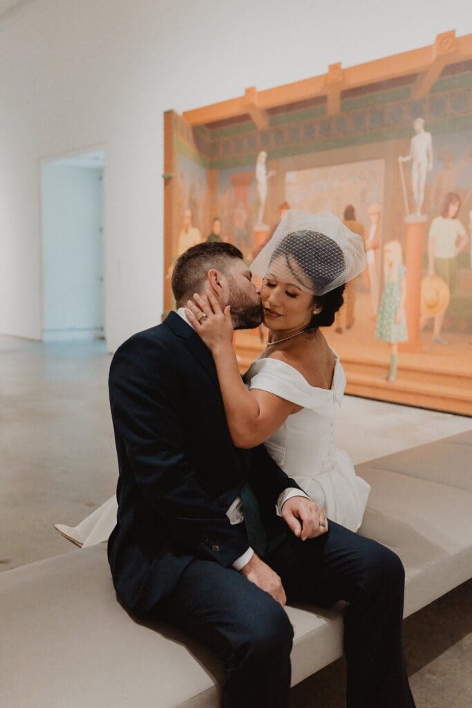 bride and groom kiss on a bench in an art gallery at the Norton Museum of Art in West Palm Beach, captured by Gracie May Photography