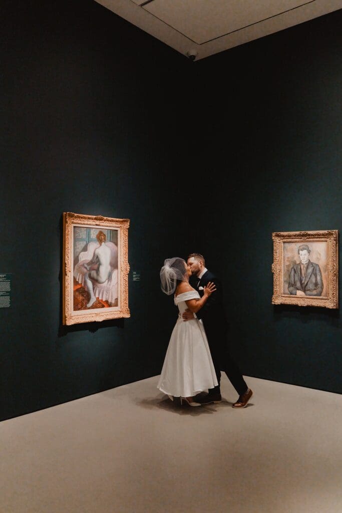 bride and groom kiss in front of two pieces of gold-framed art at the Norton Museum of Art in West Palm Beach, captured by Gracie May Photography