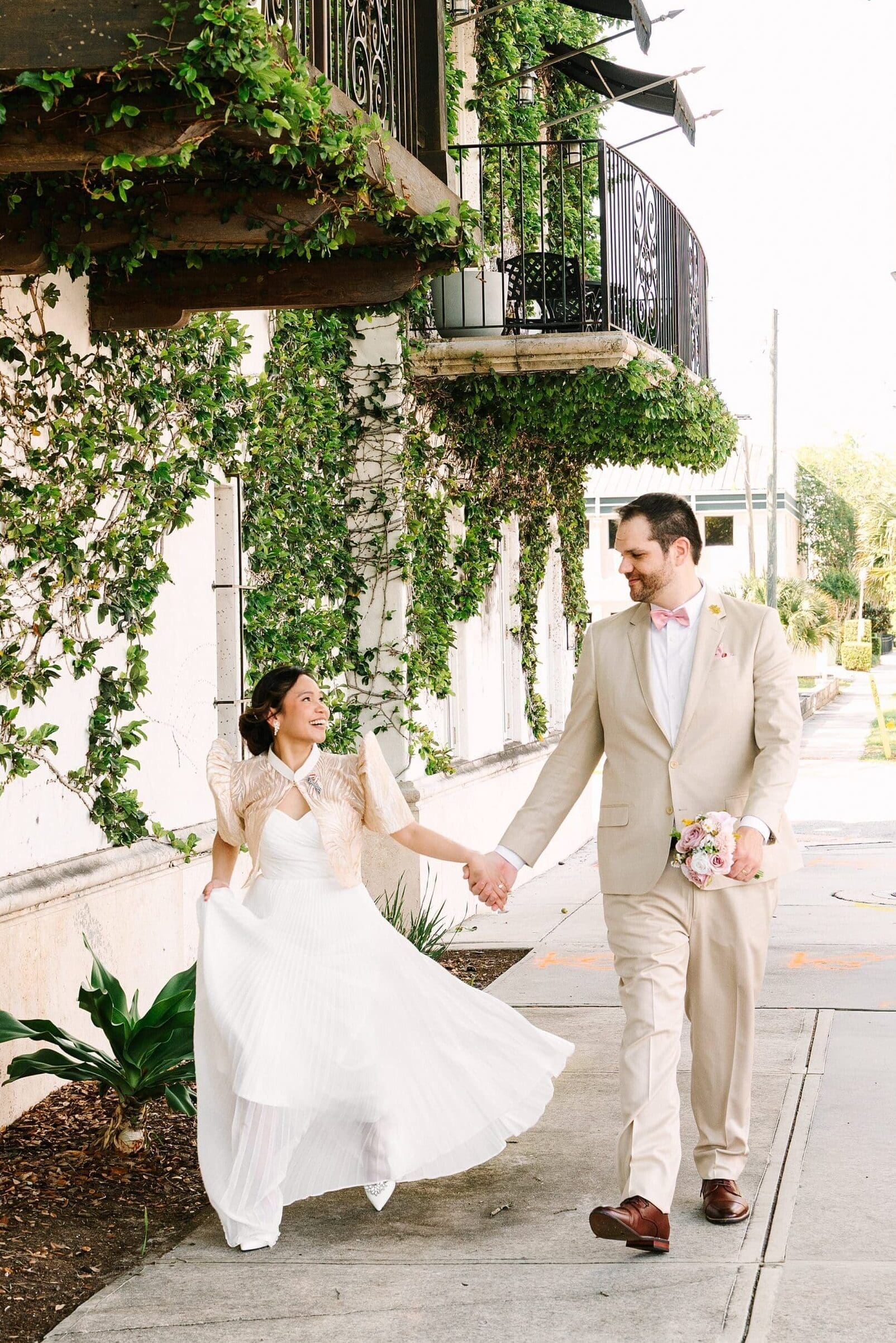 bride in a white dress with a Filipino style jacket and groom in a tan linen suit walking down the sidewalk in Winter Park Florida, captured by Gracie May Photography