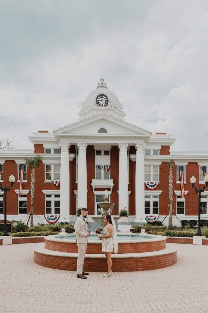 bride and groom saying their vows in front of the fountain outside of the historic Pasco County Courthouse in Dade City Florida during their outdoor wedding, captured by Gracie May Photography