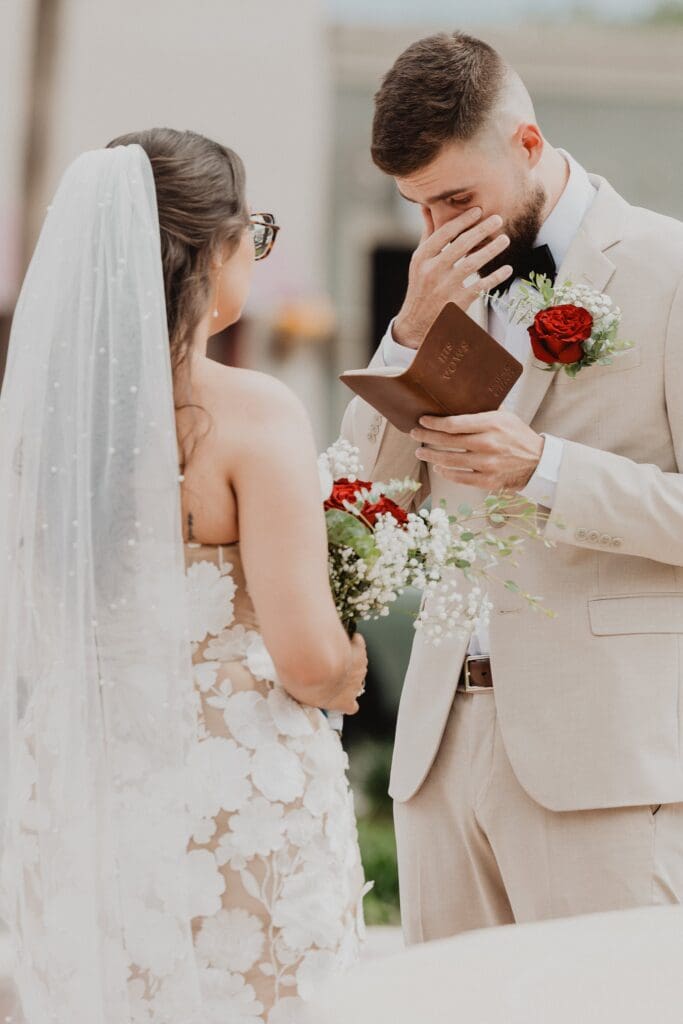 groom wiping tears while reading out of a vow book outside of the historic Pasco County Courthouse in Dade City Florida during their outdoor wedding, captured by Gracie May Photography