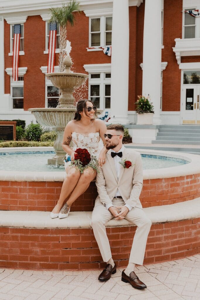 bride and groom wearing sunglasses sitting casually on the fountain outside of the historic Pasco County Courthouse in Dade City Florida after their outdoor wedding, captured by Gracie May Photography