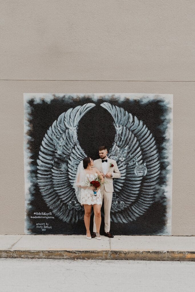 bride and groom posing in front of a mural of large wings in downtown Dade City Florida after their outdoor wedding, captured by Gracie May Photography