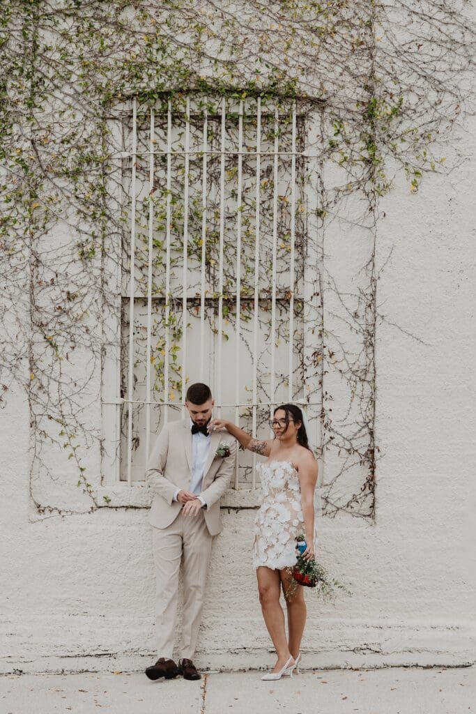 bride and groom leaning casually in front of a wall with vines in downtown Dade City Florida after their outdoor wedding, captured by Gracie May Photography