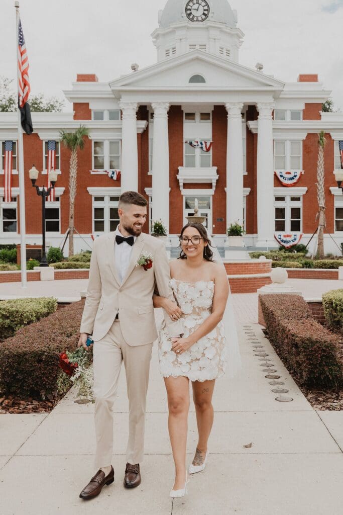 bride and groom walking while holding hands outside of the historic Pasco County Courthouse in Dade City Florida after their outdoor wedding, captured by Gracie May Photography