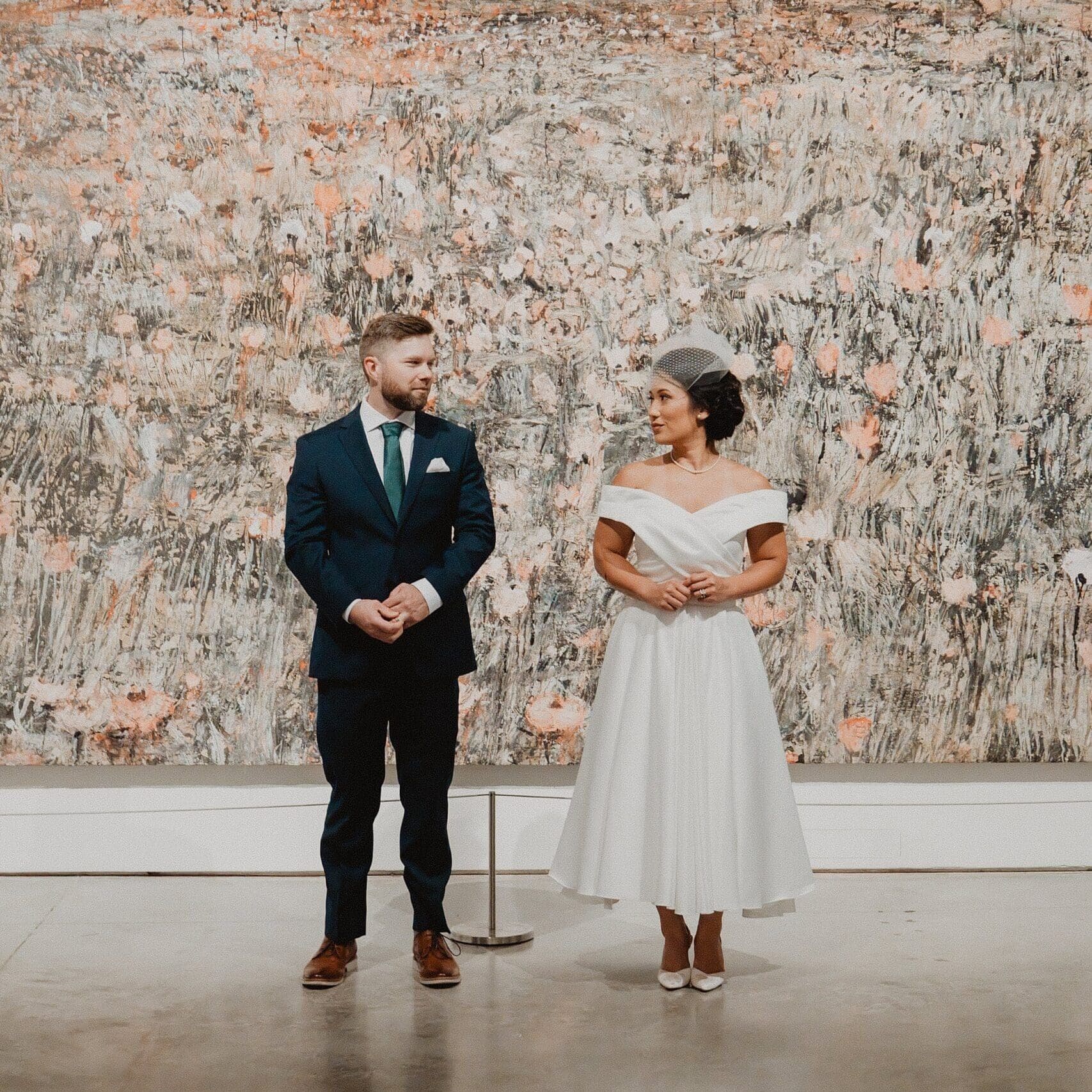 bride and groom stand and look at each other in front of a large piece of pink and gray abstract contemporary art at the Norton Museum of Art in West Palm Beach, captured by Gracie May Photography